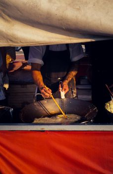 Street vendor cooking in a large wok at an outdoor market stall, wearing an apron.