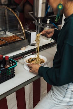 Person enjoying delicious noodles at a bustling street food stall.