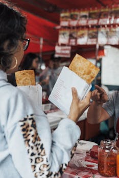 A woman holding pastries in a local market setting, engaging in casual shopping with a vendor.