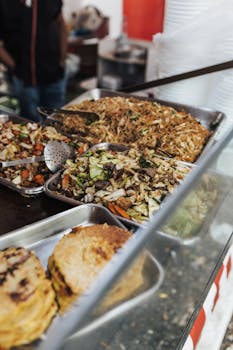 An array of delicious street food including stir-fried noodles and vegetables at a market stall.
