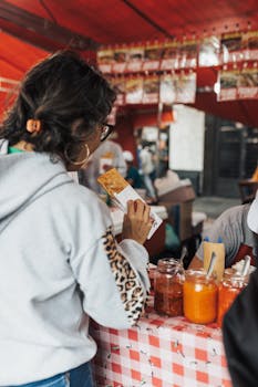 Woman holding food at a lively street food market with various sauces displayed.