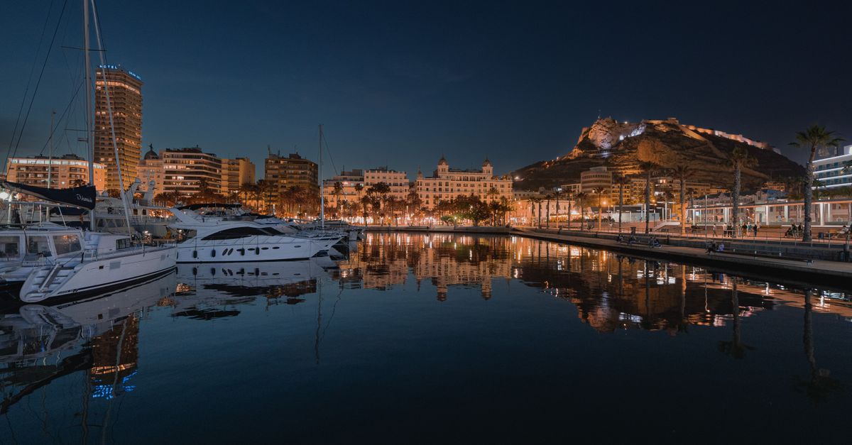 Illuminated Alicante harbor at night showcasing the skyline and the historic Santa Bárbara Castle reflection.