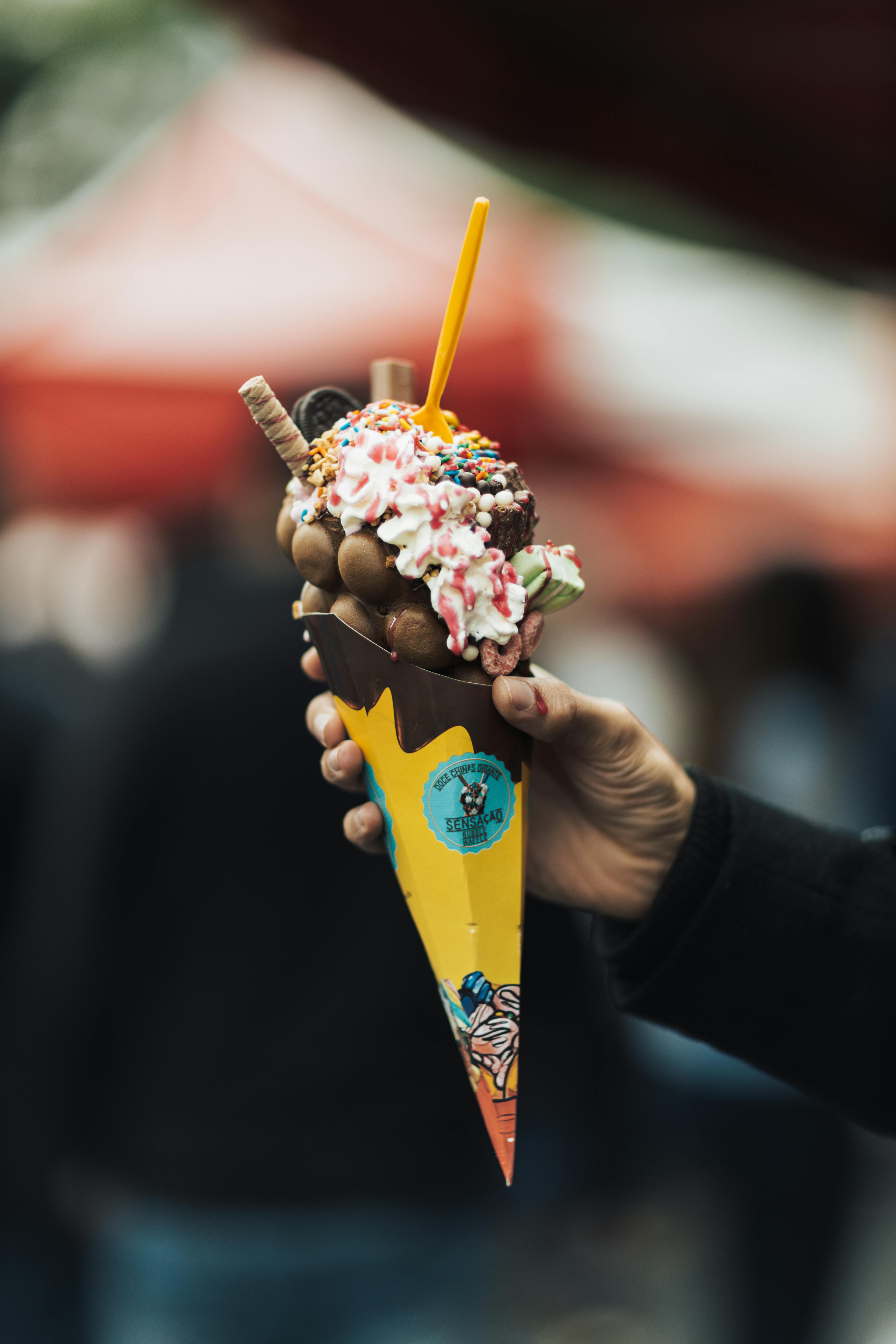 Hand holding a bubble waffle dessert with chocolate and sprinkles, perfect for food lovers.