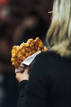 A woman with blonde hair holding and eating a waffle on a city street.
