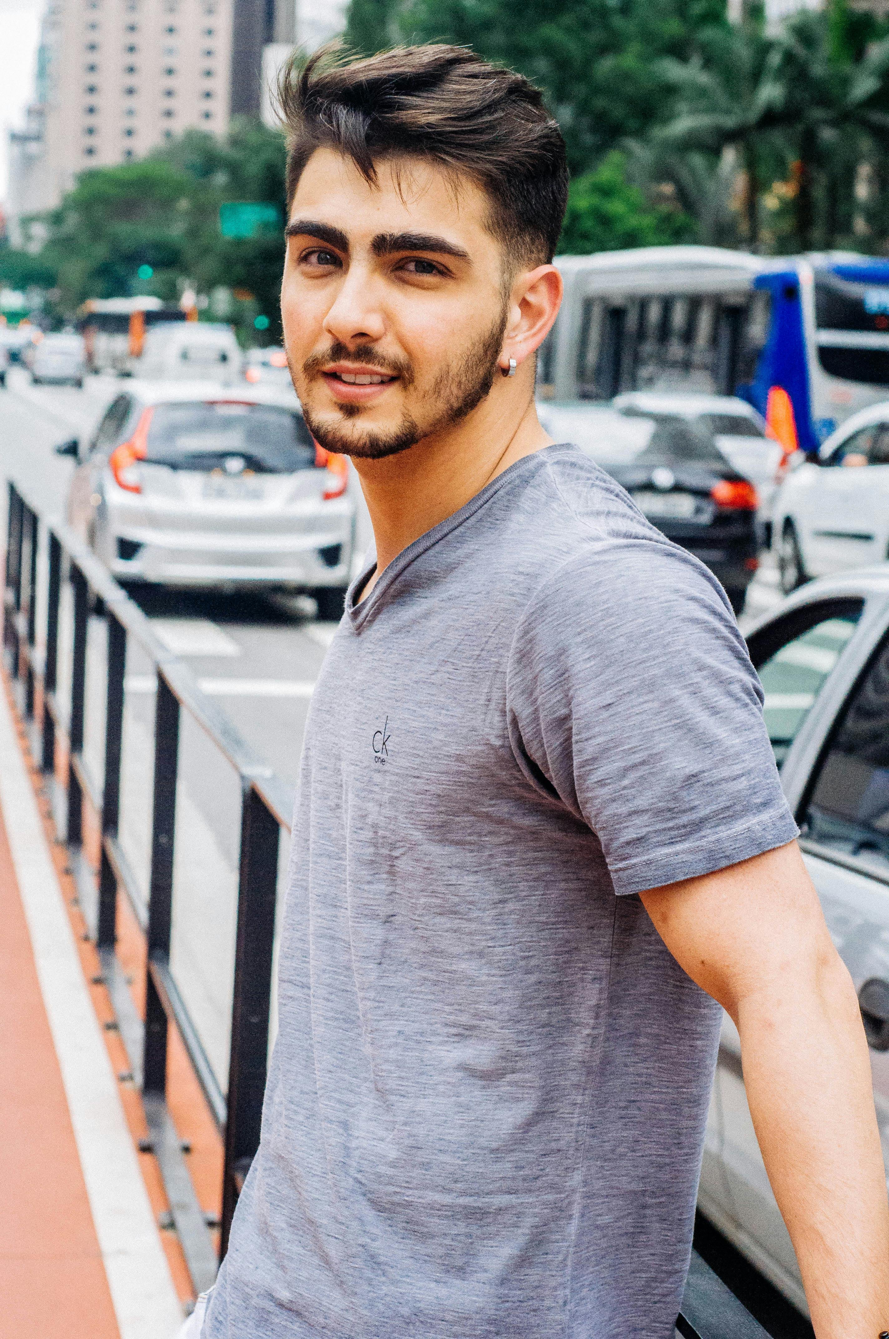Stylish young man with facial hair in an urban street scene wearing a gray t-shirt.