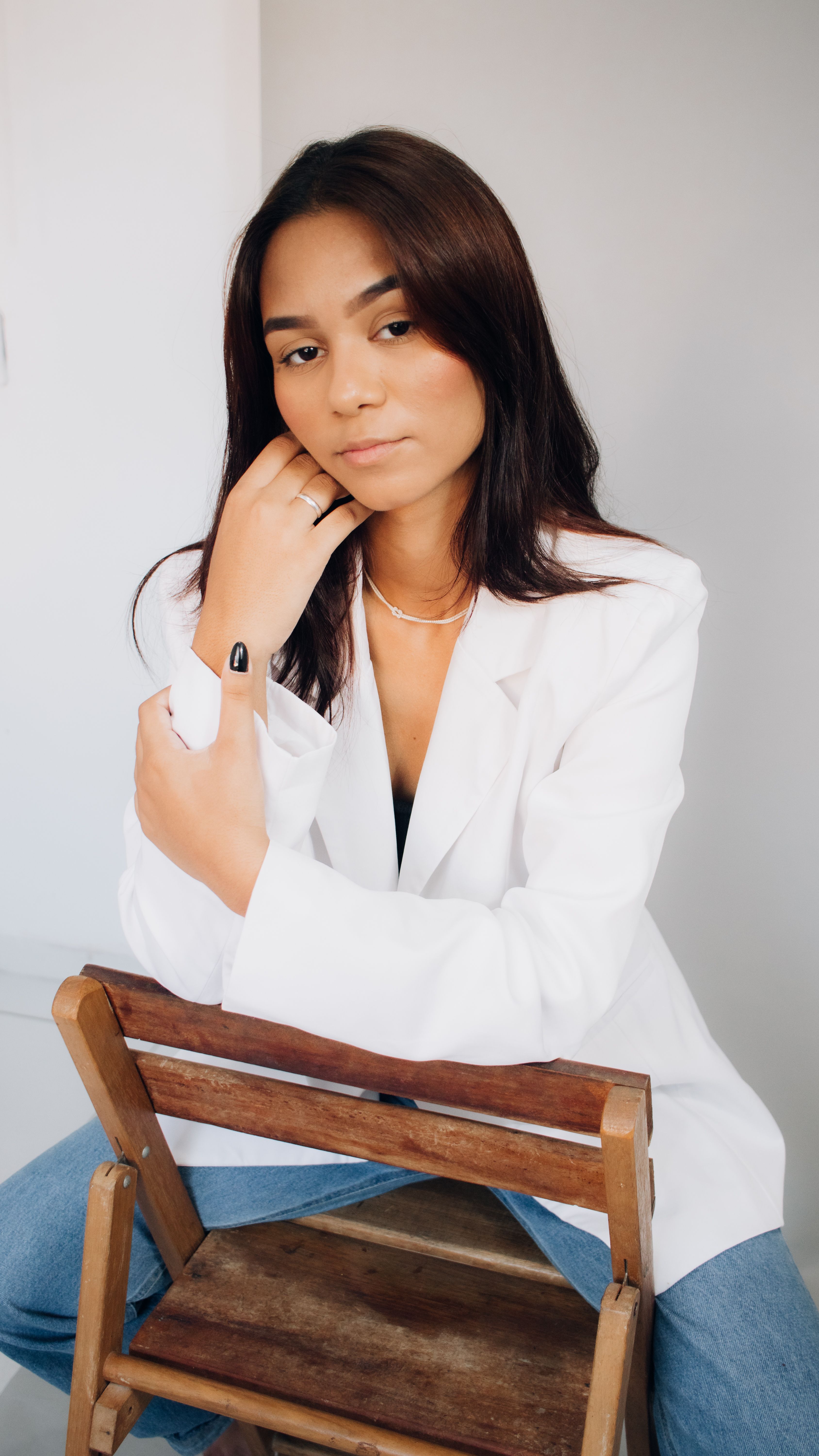 Portrait of a woman with long brunette hair in a white jacket, posing confidently indoors.