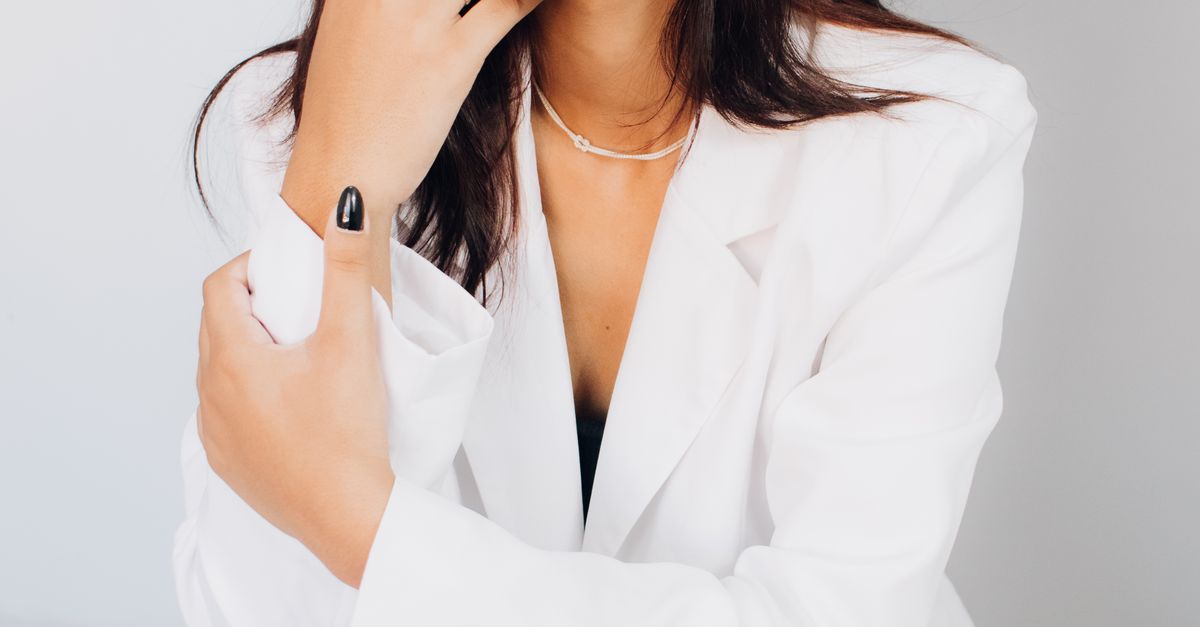 Portrait of a woman with long brunette hair in a white jacket, posing confidently indoors.