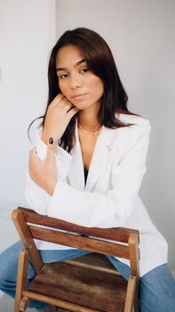 Portrait of a woman with long brunette hair in a white jacket, posing confidently indoors.