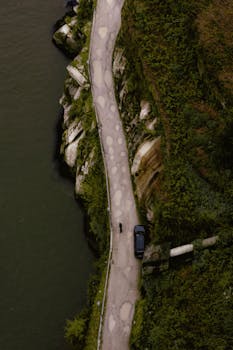 Dramatic aerial shot of a coastal road with a parked vehicle, capturing the natural landscape and scenic views.