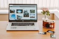 工作空间干净时尚，配有笔记本电脑、宝丽来照片和沐浴在自然光线下的开花植物