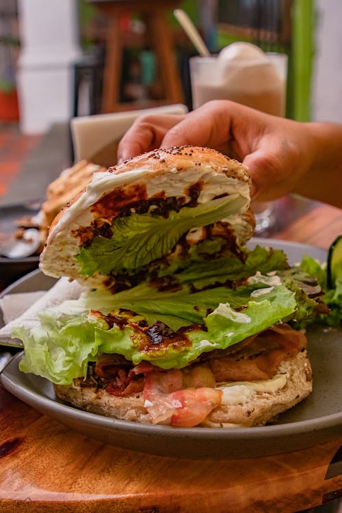 A person holding a sandwich with lettuce and cheese