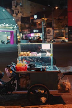 A bustling nighttime street food cart with vibrant city lights and urban backdrop.