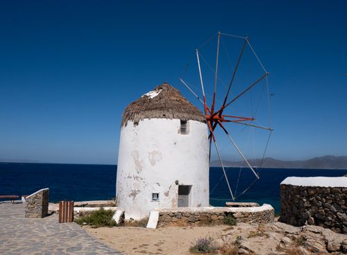 Free Iconic windmill on a sunny day in Mykonos, Greece, with a clear blue sky and the Aegean Sea. Stock Photo