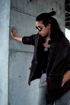 一名穿着街头服饰的妇女若有所思地站在混凝土墙上，目光移开