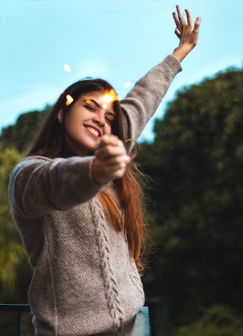 бесплатная Выборочный фокус фотография улыбающейся женщины, держащей зажженный бенгальский огонь, позирующей с поднятой рукой Стоковое фото
