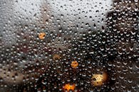 这张迷人的宏观照片捕捉了窗户上的雨滴，背景是模糊的城市灯光