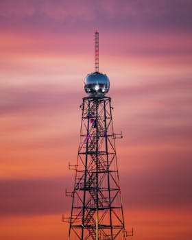 一座著名的通信塔矗立在充满活力的日落天空下，展现了现代电信技术