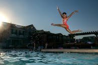 日落时分，一名穿着泳衣的年轻女孩跳进游泳池，享受夏日乐趣