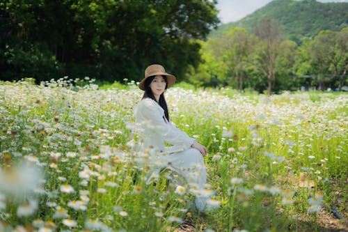 A woman in a white hat sits in a field of flowers