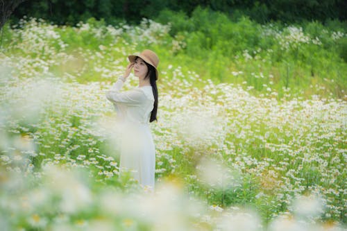 A woman in a white dress is standing in a field of flowers