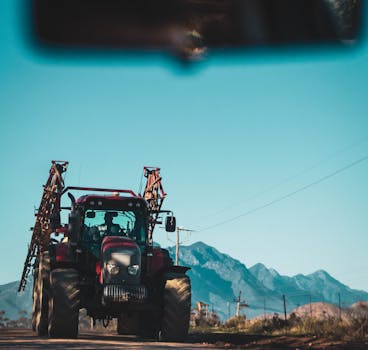在山区背景下的乡村道路上，停着一辆红色拖拉机，体现了农村交通