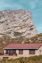 一座红色屋顶的乡村平房，在晴朗的天空下，映衬着崎岖的岩石山脉