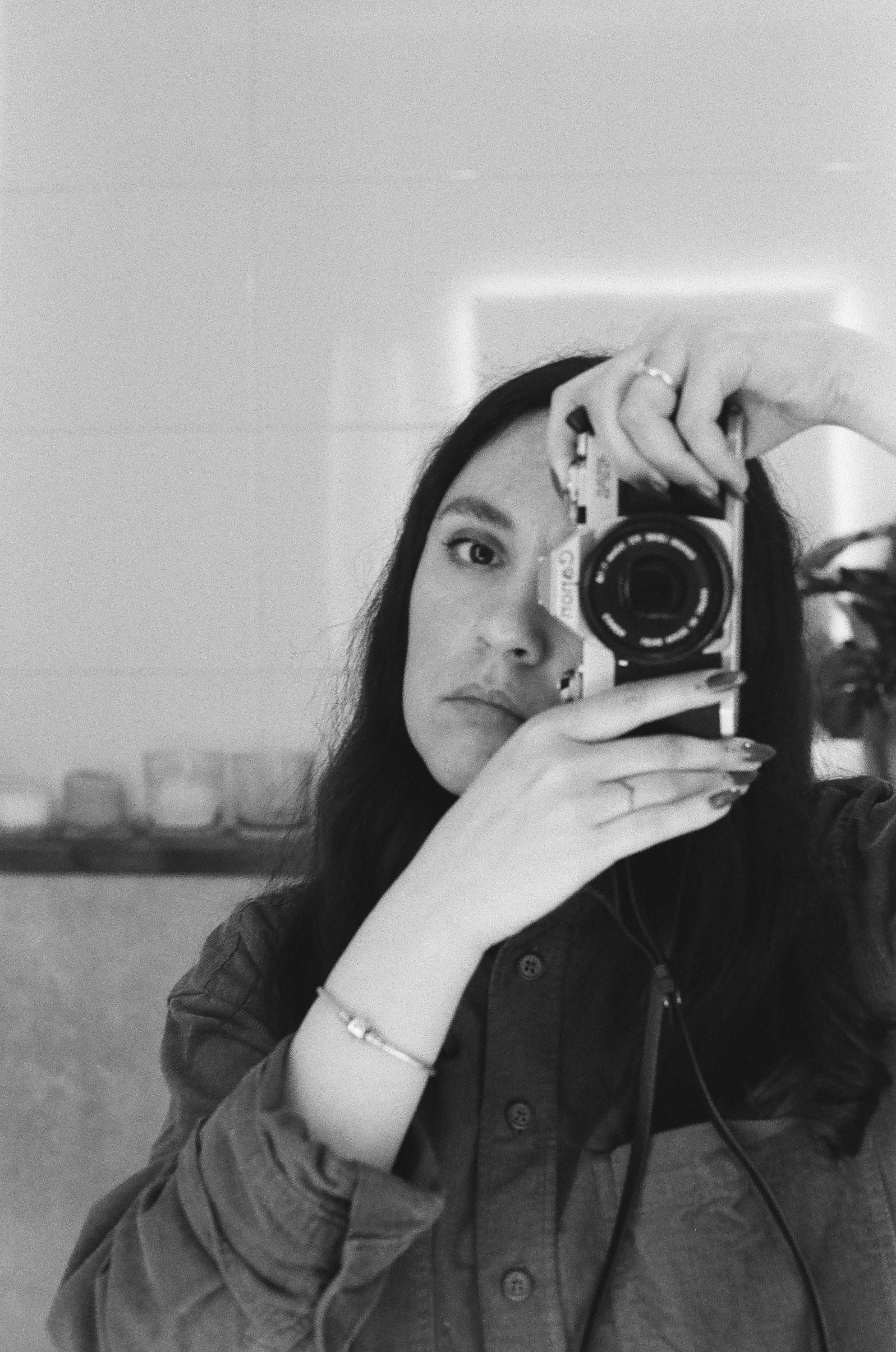Black and white photo of a woman taking a self-portrait with a vintage analog camera.