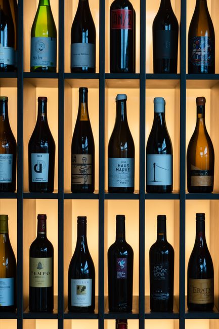 A vertical arrangement of diverse wine bottles on a backlit shelf displaying elegance and variety.
