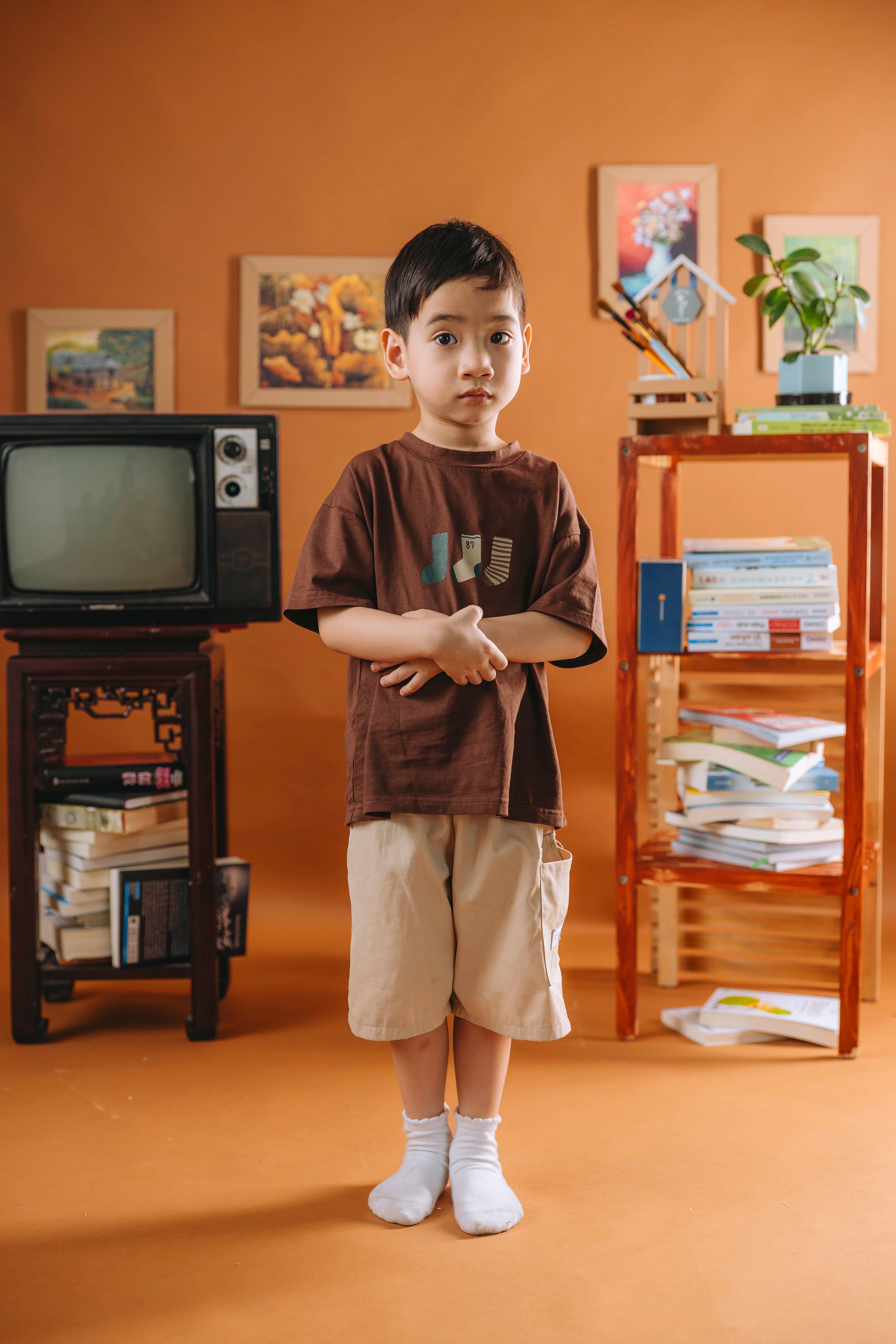 Asian boy standing in a vintage-inspired room with orange decor, TV, books.