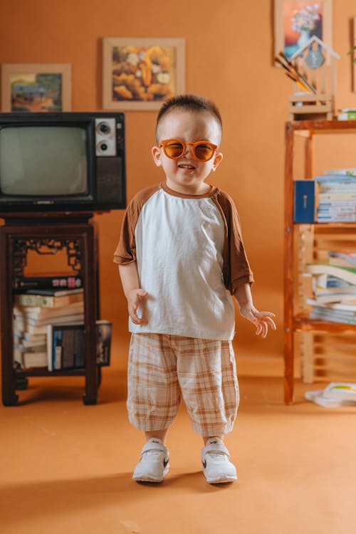 A baby wearing sunglasses and a shirt standing in front of a television