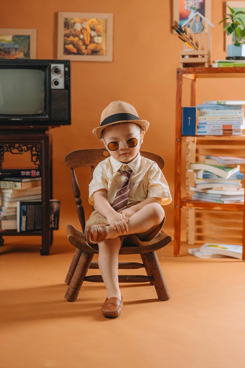 A little boy in a hat and sunglasses sitting on a chair