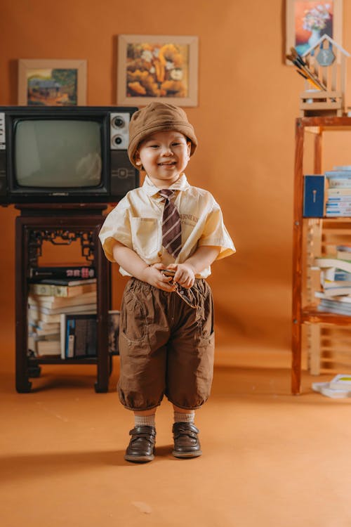 A little boy in a hat and tie standing in front of a television