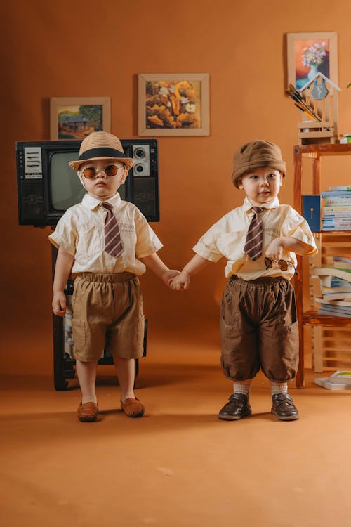 Two children dressed in hats and ties holding hands