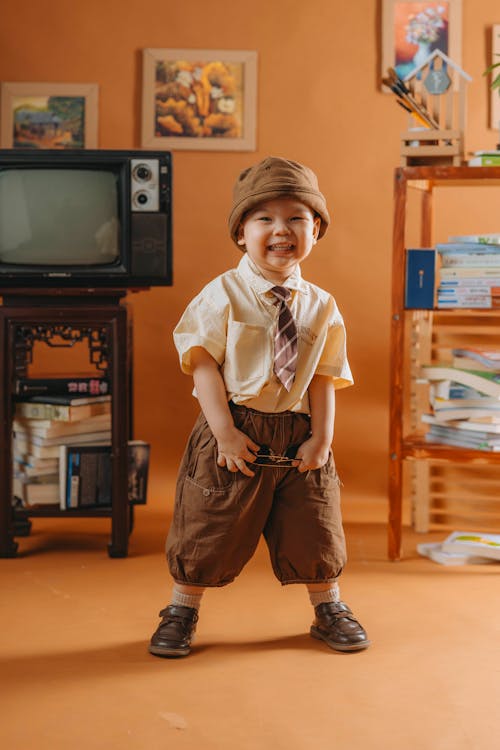 A little boy in a hat and tie standing in front of a television
