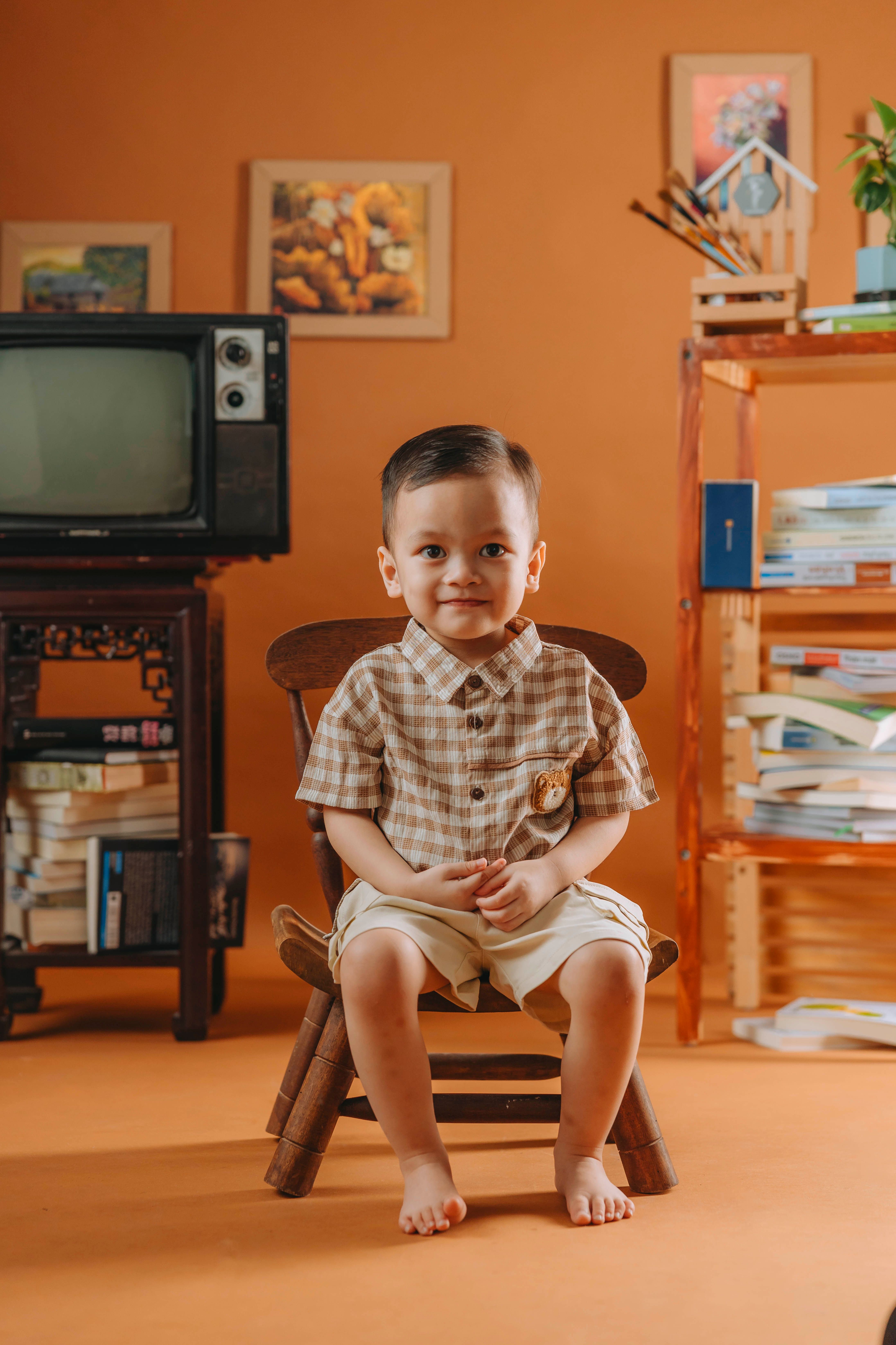 Adorable toddler sitting on a wooden chair in a retro-styled orange room.