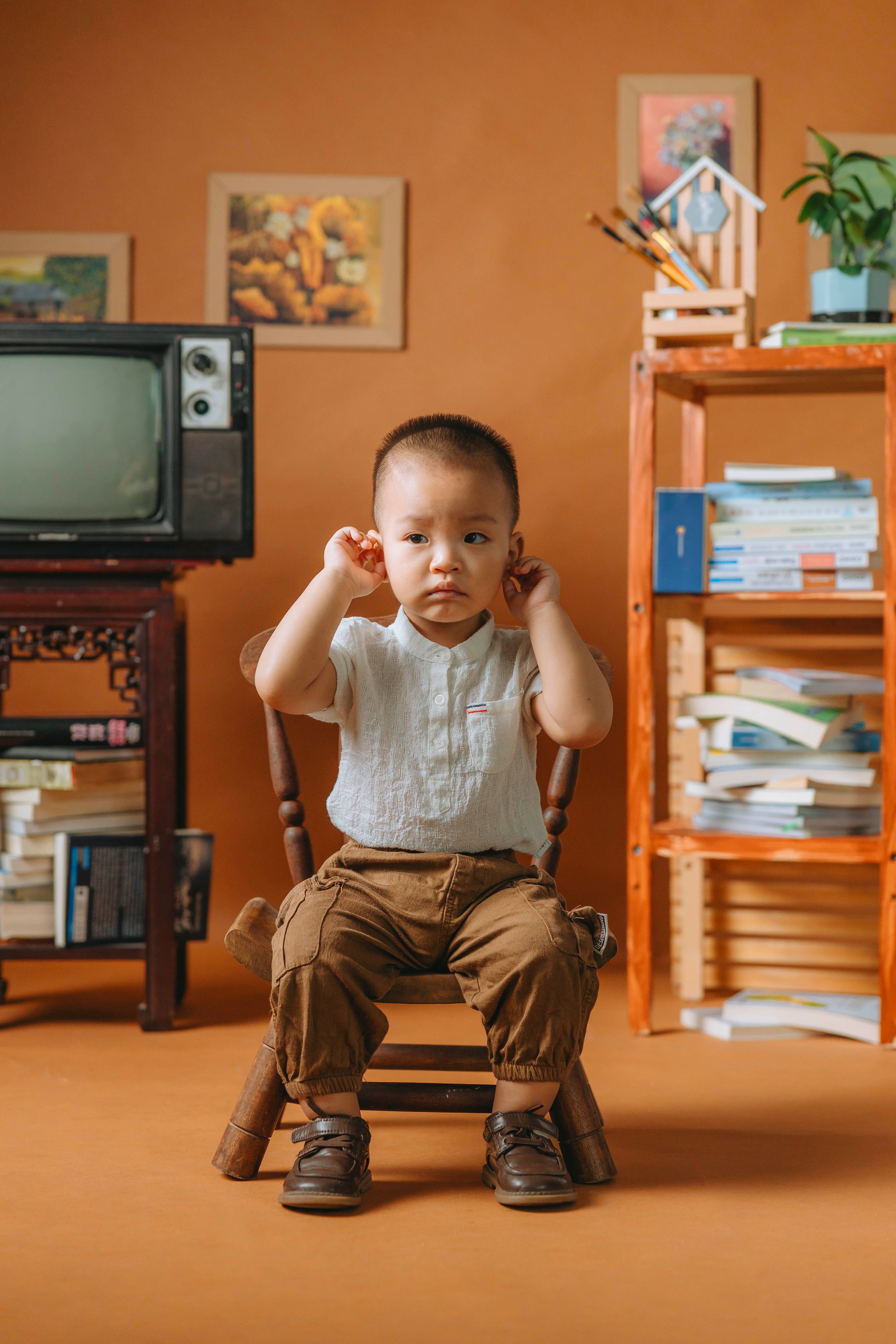 Adorable child in elegant clothes sitting in a cozy, vintage-styled room with wooden furniture.