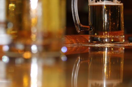 Free Golden beer mug with frothy head and reflection on a wooden bar table. Stock Photo