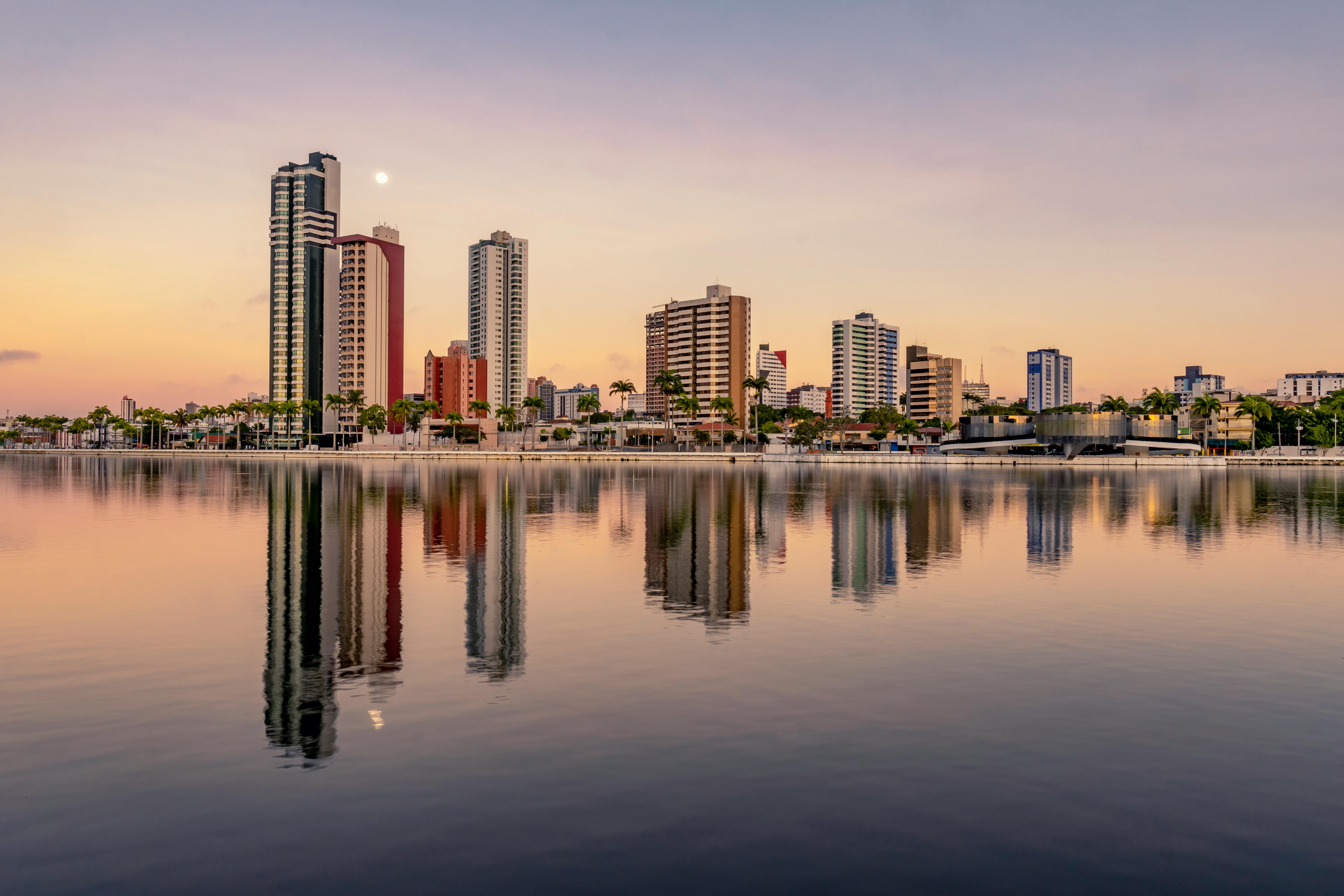 Picturesque scenery of coherent tall modern buildings of contemporary megalopolis near calm river in sunset in dusk