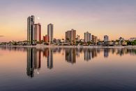 Picturesque scenery of coherent tall modern buildings of contemporary megalopolis near calm river in sunset in dusk