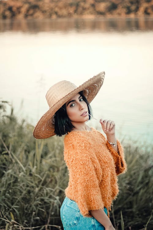 Photo of Woman in Beige Sun Hat, Orange Knitted Top and Blue Denim Bottoms