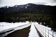一辆充满活力的黄色汽车，在雪山道路上格外显眼，四周环绕着常绿树木和山峰