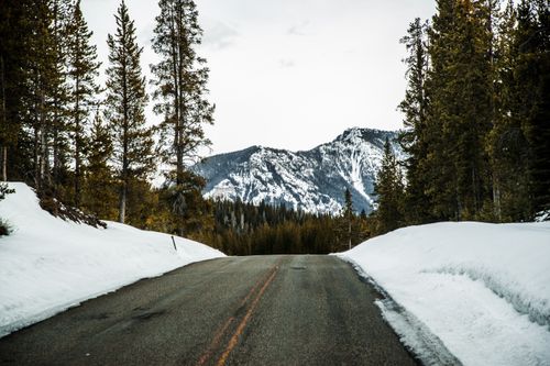 Free Scenic mountain road flanked by snowy coniferous forest and distant peaks. Stock Photo