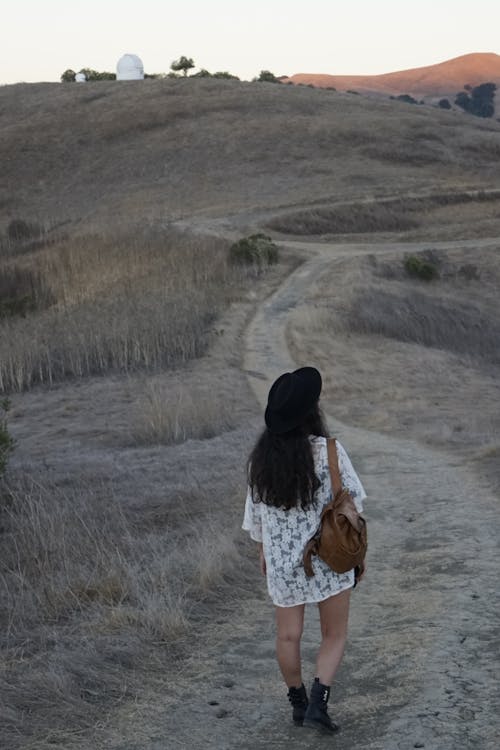 Back View Photo of Women Walking Down Dirt Road Carrying Brown Bag