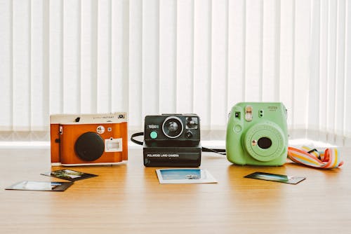 Drei Verschiedene Sofortbildkameras Mit Beispielfotos Auf Dem Tisch