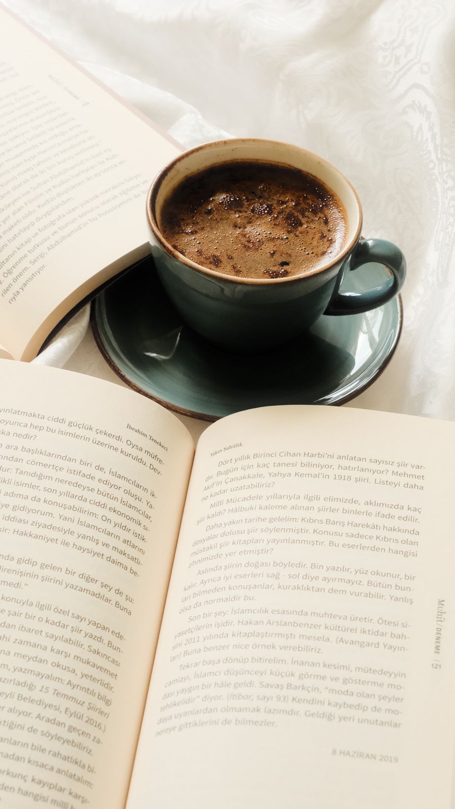 An open book lying flat beside a cup of coffee and a pair of glasses