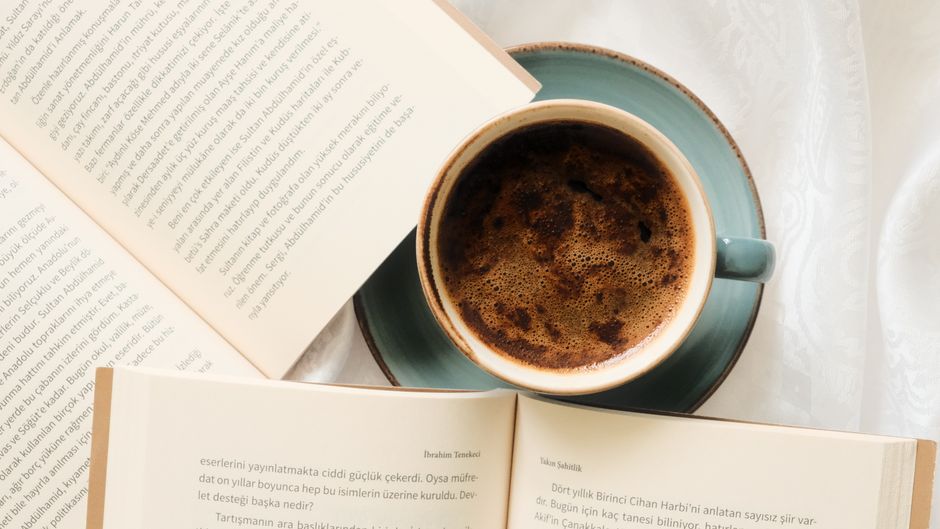 A comforting scene with a coffee cup and open books on a soft white background.