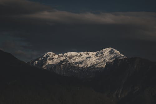 A mountain with snow capped peaks under a dark sky