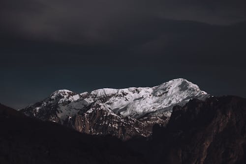 A dark cloudy sky with snow capped mountains