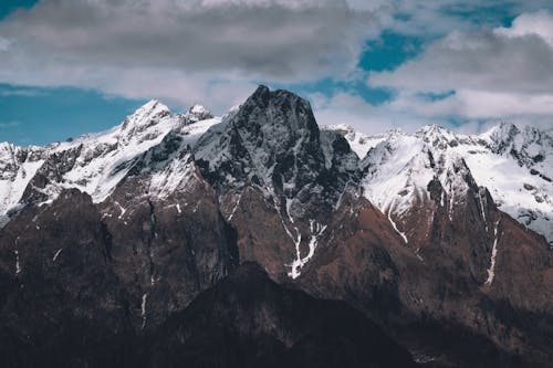 A mountain range with snow capped peaks under a cloudy sky