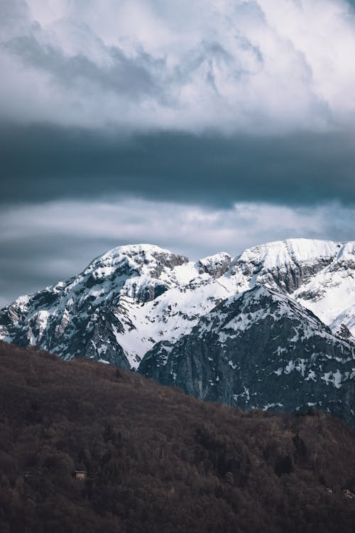 A mountain range with snow covered peaks under a cloudy sky
